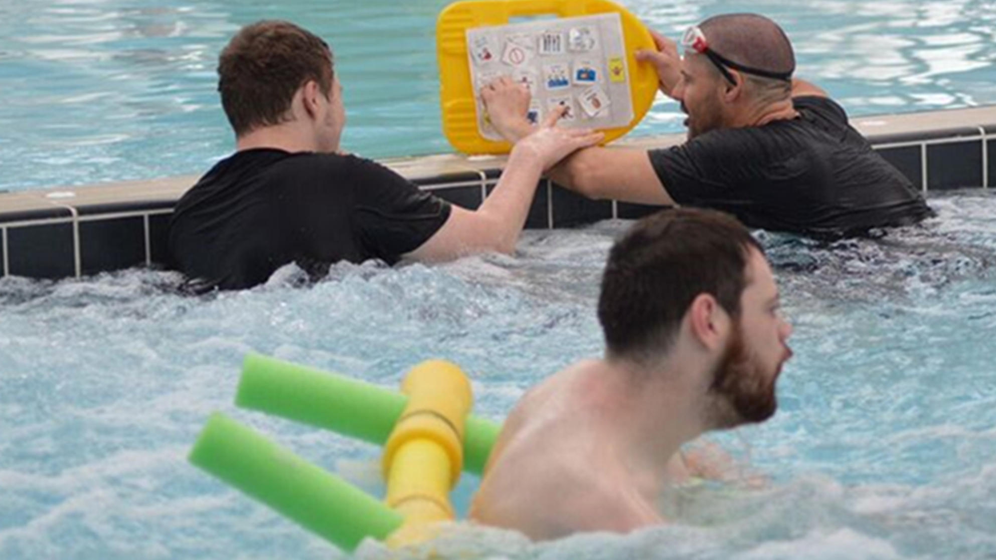 Three men enjoying some leisure time in the pool. Two of them are chatting using a communication display stuck on a kick board.