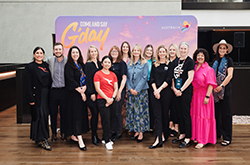 Tourism Australia staff standing in front of a a 'Come and Say G'day' campaign promotional banner