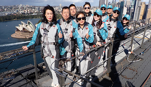 Corporate clients from Greater China posing for a photo at the top of the Sydney Harbour Bridge, with the Opera House and city in the background © Tourism Australia