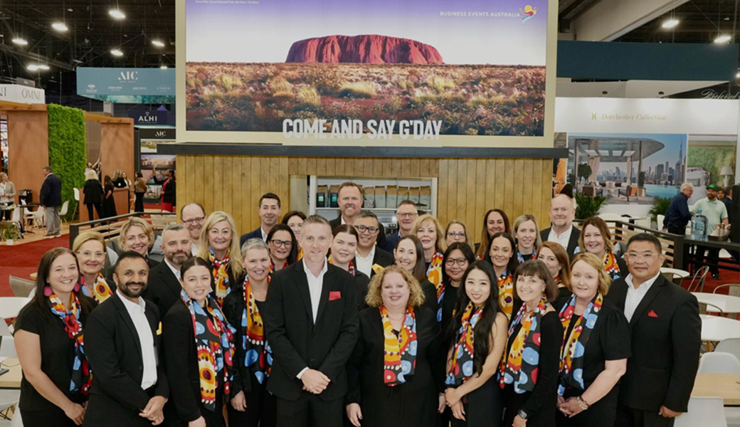 Australian industry standing for a group photo at the Australia stand with an image of Uluru above them