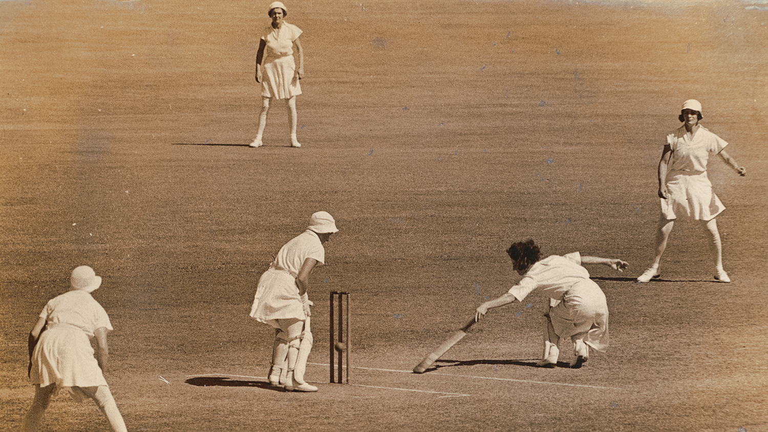 A sepia photograph of three women playing cricket.