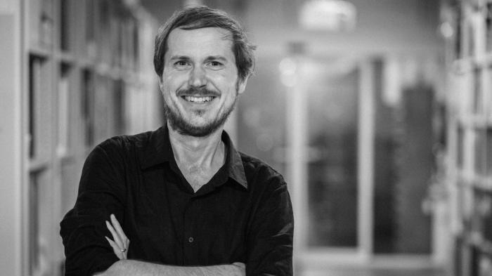 A black and white photo of a man smiling with his arms crossed.