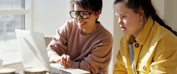 This is a photo of a lady with a teenage female with Down syndrome using a laptop