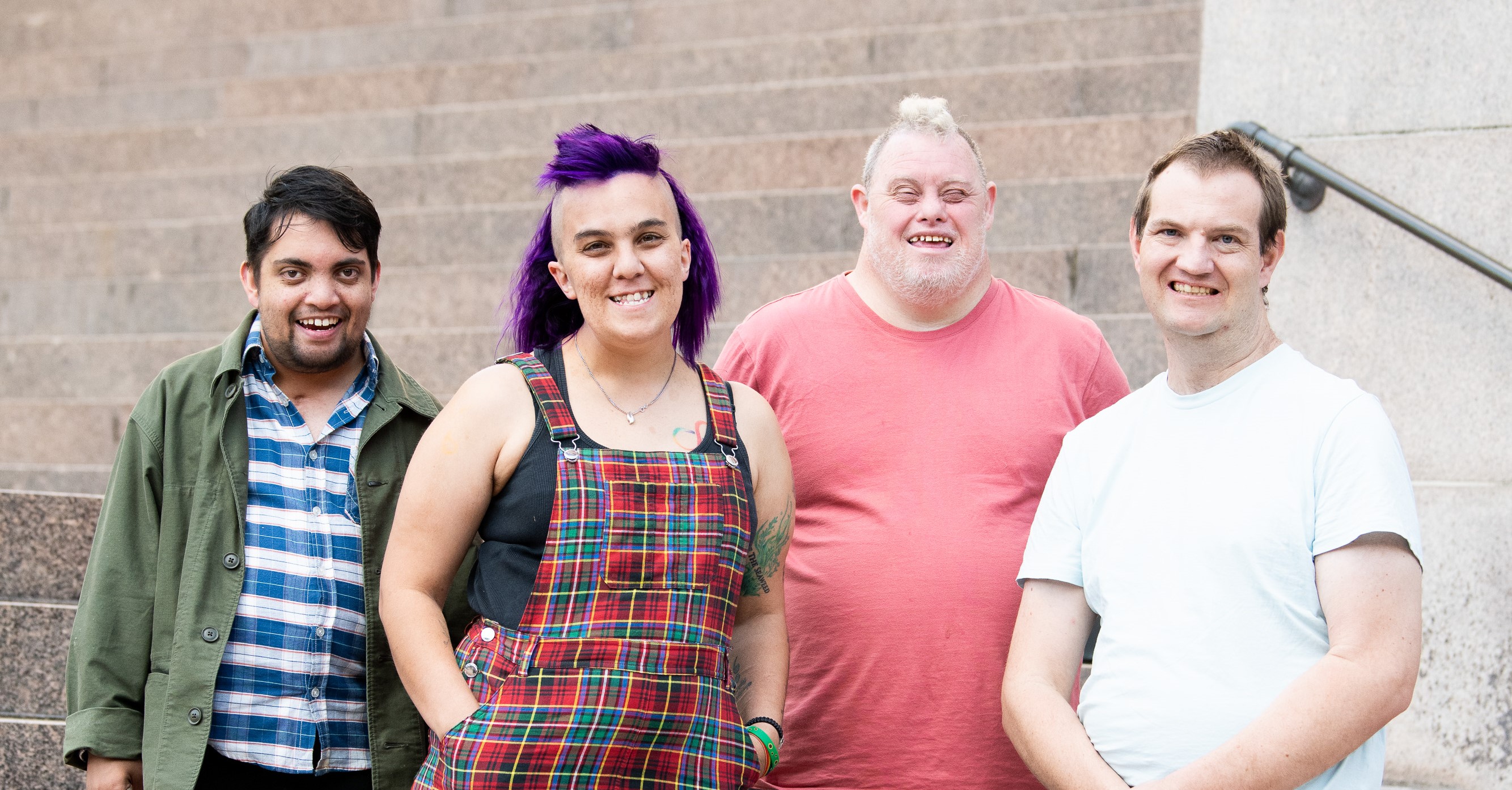 This is a photo of four people with intellectual disability smiling. Three males and a female