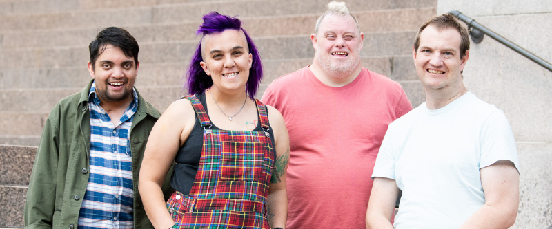 This is a photo of three males and one female with intellectual disability smiling at the camera.