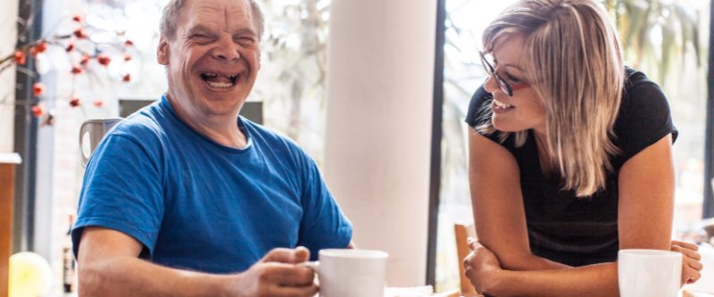 This is a photo of a man with Down syndrome smiling next to his female carer