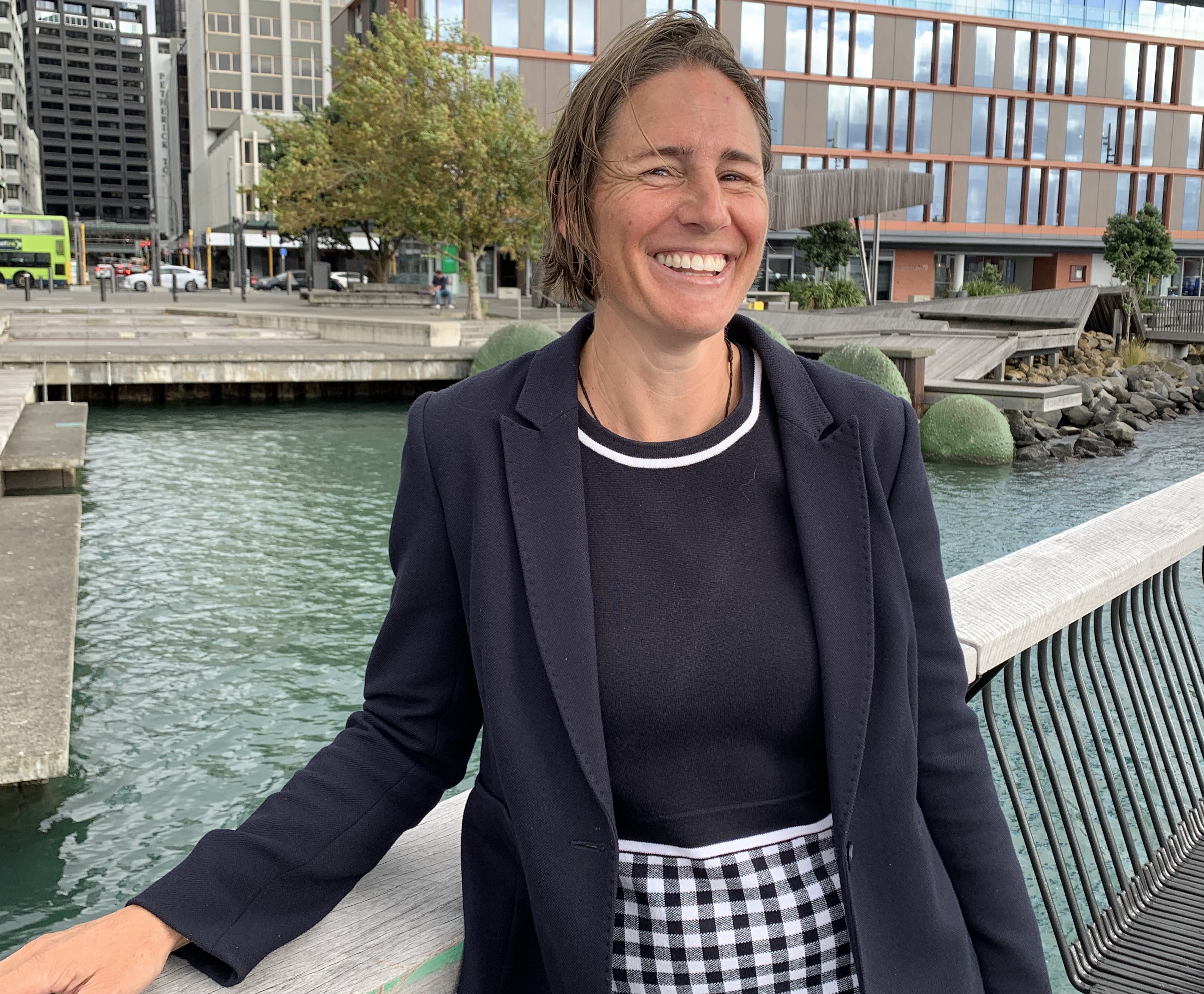 Sophia Hadef, of Keystone Procurement. She is standing in front of a garden fence with her arms crossed. She is wearing a jacket and a necklace.
