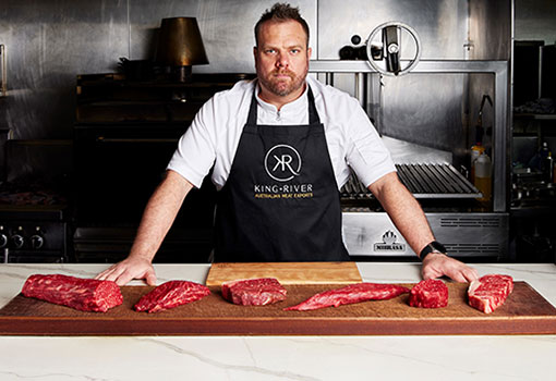 Butcher in kitchen with various cuts of beef