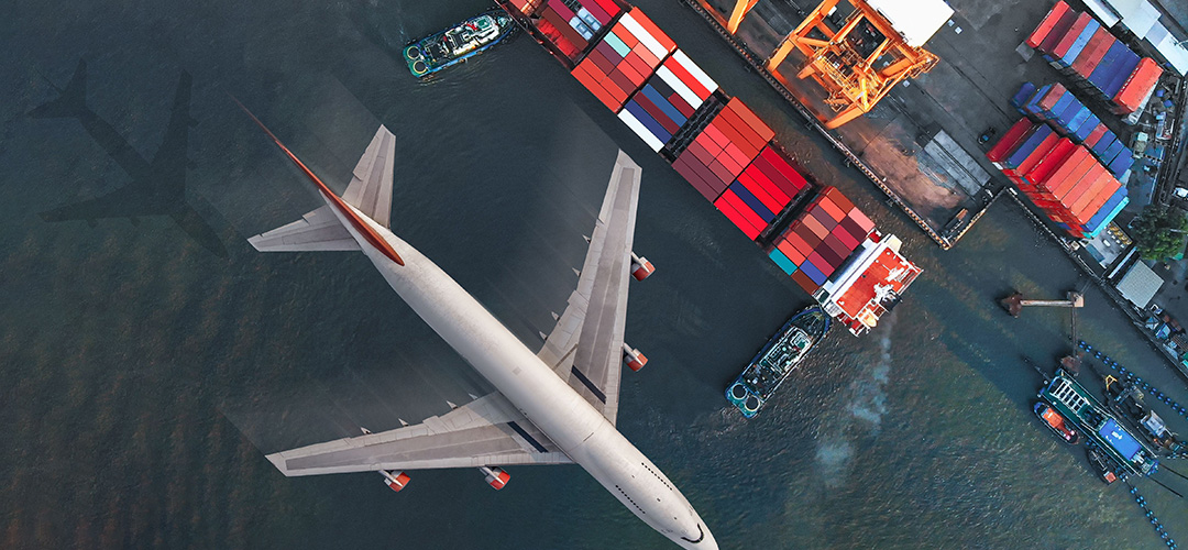 Plane flying over cargo ship passing through a port