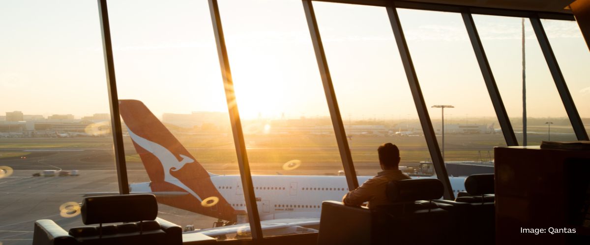 A man in an airport lounge looks over the tarmac and the tail of a Qantas plane.. Image: Qantas