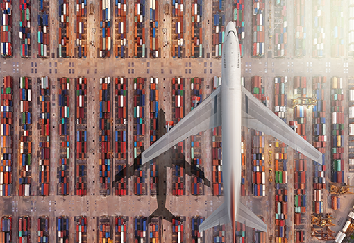 Aerial view of cargo plane flying over port with shipping containers